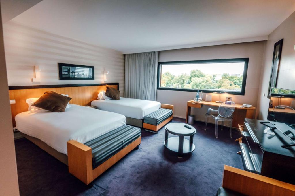 a hotel room with two beds and a desk at Hotel Lille Euralille - Hilton Affiliate Hotel in Lille