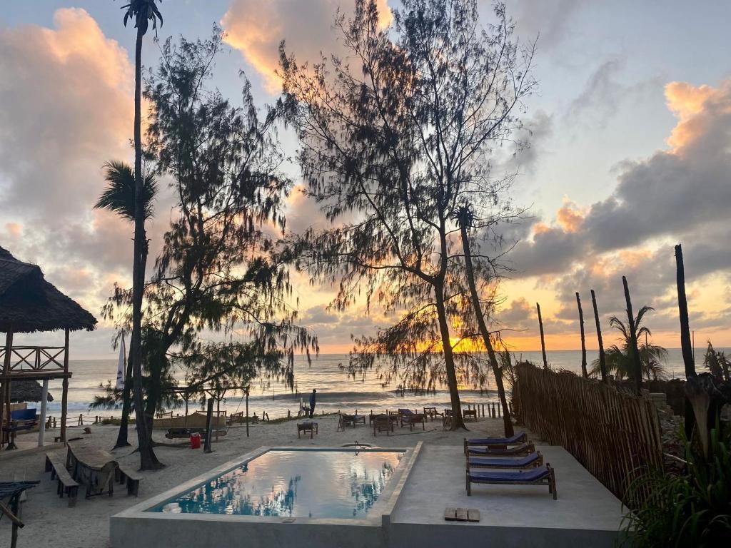 a pool on the beach with a sunset in the background at Drifters Zanzibar in Paje