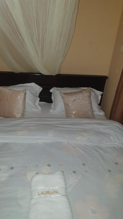 Una cama con sábanas blancas y almohadas. en LAURAPA home's, en Kisumu