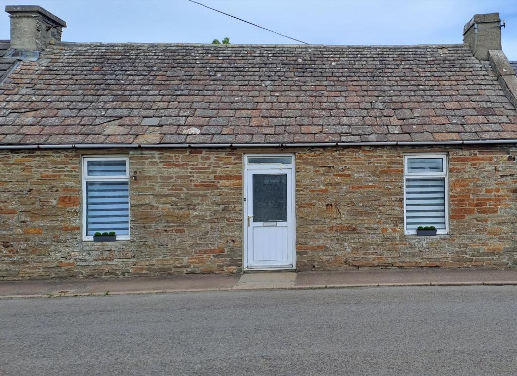 un edificio de ladrillo con una puerta y ventanas blancas en Riverview Cottage, en Halkirk