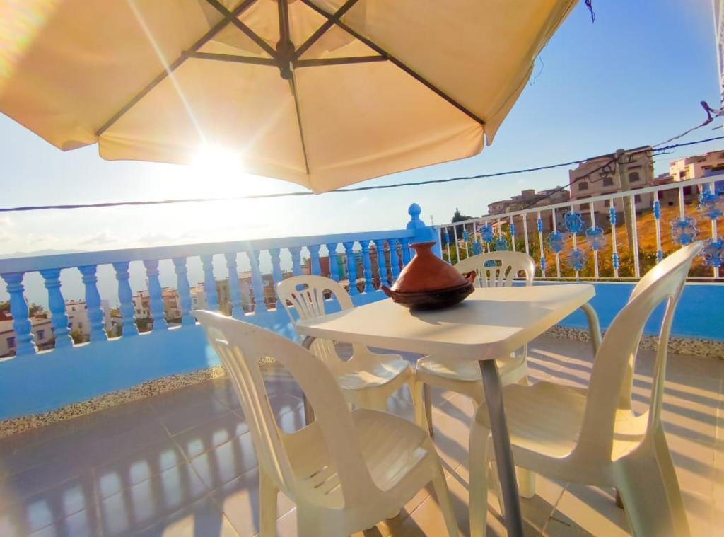 d'une table et de chaises blanches avec un parasol sur le balcon. dans l'établissement Dar Khairoun with Parasole, à Chefchaouen