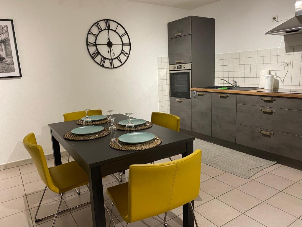 a kitchen with a table with yellow chairs and a clock at Les pampas in Montbronn