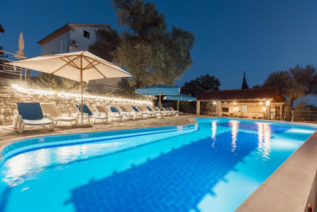 a swimming pool with chairs and an umbrella at Villa Mia Apartments in Bijela