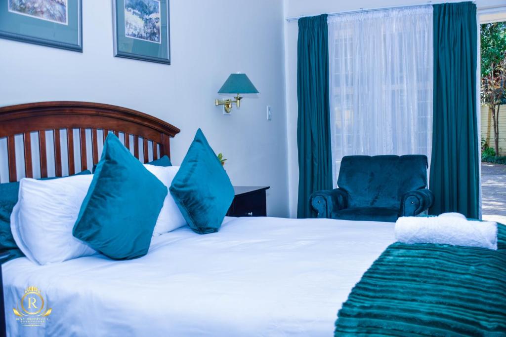 a bedroom with a bed with blue pillows and a chair at Royal Highness Lux Guesthouse in Carletonville
