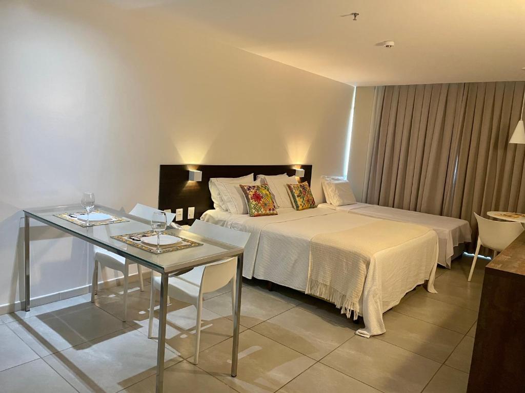 una camera d'albergo con letto e tavolo in vetro di Coral Ritz - Flat beira mar (Condomínio Ritz Suites Home Service) a Maceió