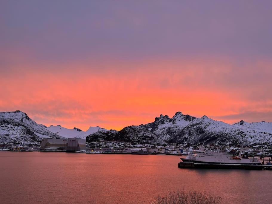 a sunset over a body of water with snow covered mountains at Sentrumsnær leilighet med utsikt in Svolvær