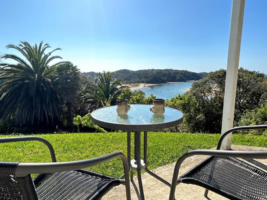 a table with two mugs on it with two chairs at Chenies Holiday Flat in Ngunguru