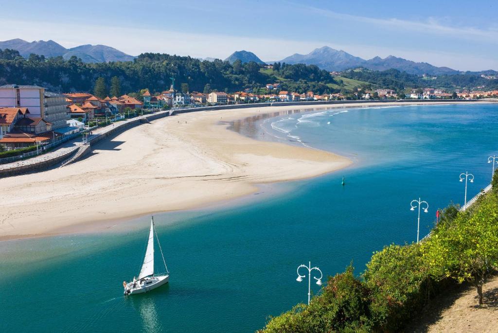 a sailboat in the water next to a beach at Apartamento Playa de La Atalaya in Ribadesella