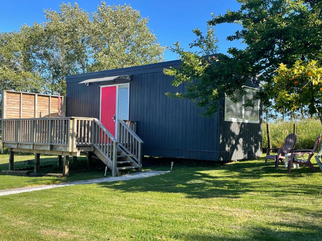 a black building with a red door and a deck at Cotman Cottage on Coatesville in Kumeu