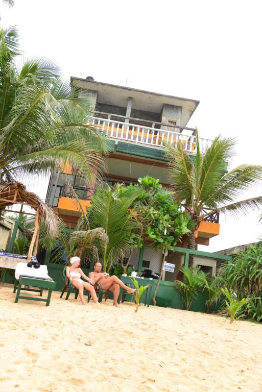Dos personas sentadas en la playa frente a un edificio en Athula Hikka beach Guesthouse, en Hikkaduwa