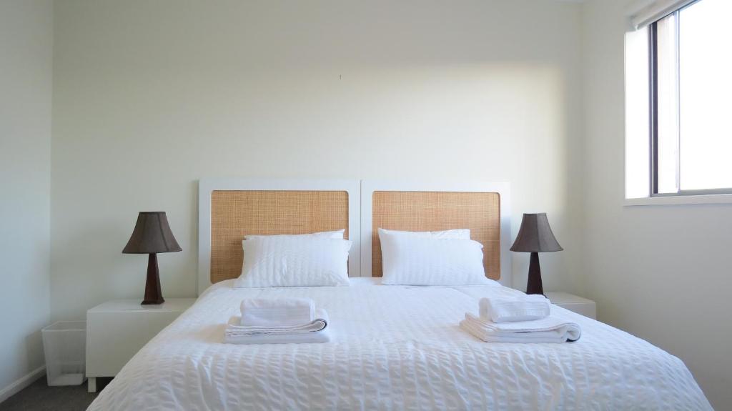 a bedroom with a white bed with two towels on it at GREENWAY WATERS Apartments in Tuggeranong