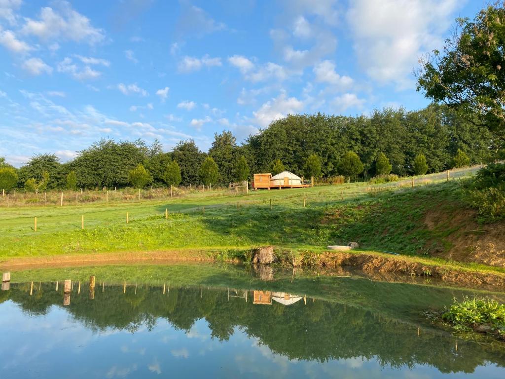 a pond in a field with a barn in the background at Bracken Yurt at Walnut Farm Glamping in Netherbury