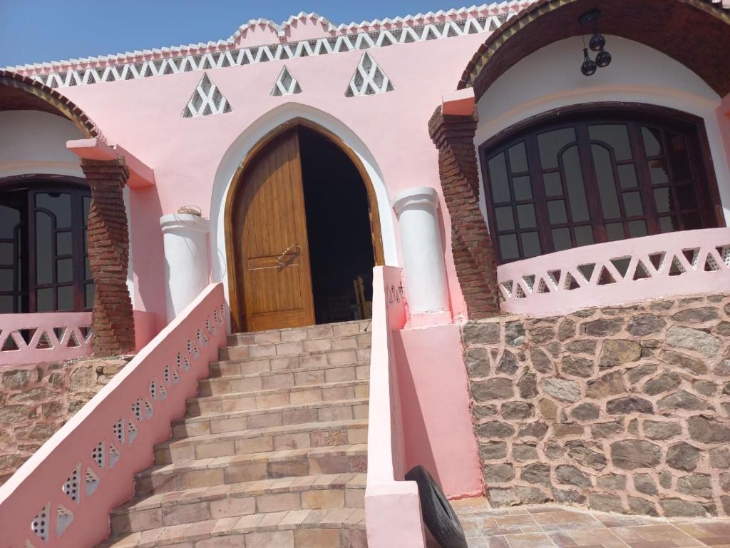różowy dom ze schodami i drewnianymi drzwiami w obiekcie Hoolli Villa w mieście Aswan