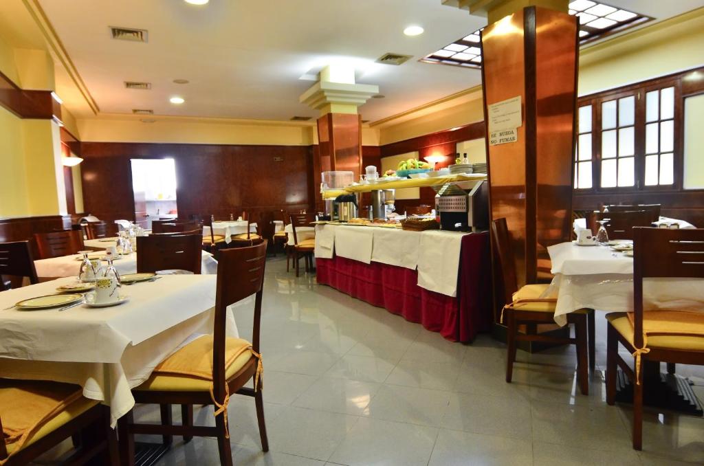 a restaurant with white tables and chairs and a counter at Hotel Jucamar in Cangas de Morrazo