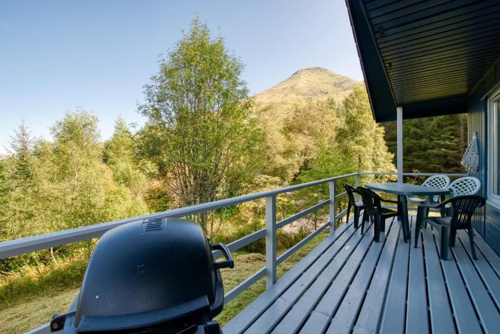 eine Terrasse mit einem Tisch, Stühlen und einem Berg in der Unterkunft 2 bedroom lodge sleeps 4 loch and mountain view in Crianlarich