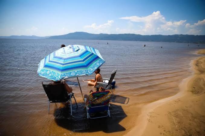 two people sitting in chairs under an umbrella on the beach at Kitnet no Centro de São Pedro da Aldeia De frente para Lagoa in São Pedro da Aldeia