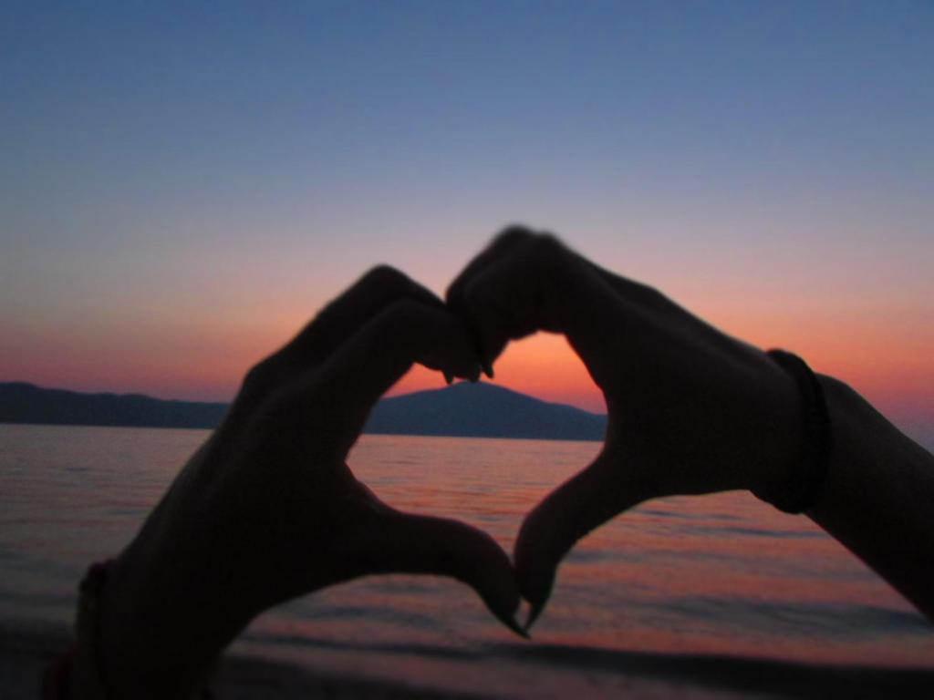 a pair of hands in the shape of a heart in front of a sunset at Blue Paradise Hotel in Orikum