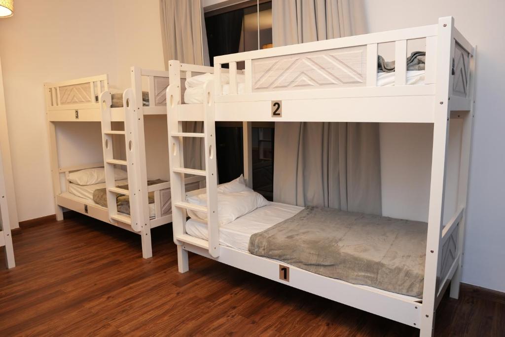 2 białe łóżka piętrowe w pokoju z drewnianą podłogą w obiekcie Shams JBR Hostel w Dubaju