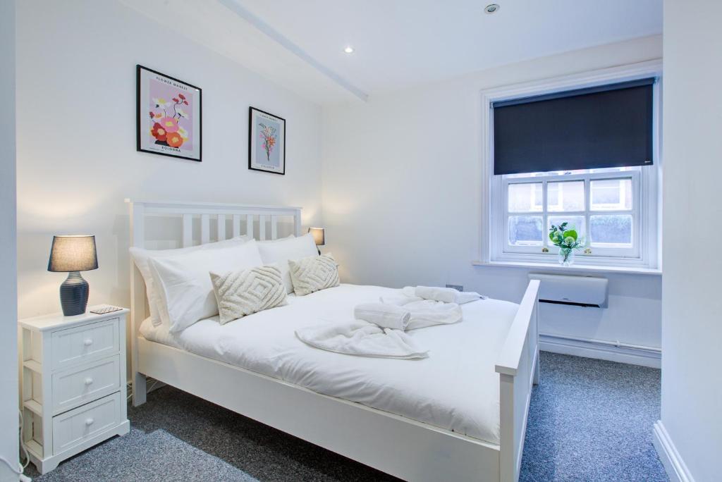 Spacious One Bedroom Apartment in The Heart Of Brentwood في برنتوود: غرفة نوم بيضاء مع سرير أبيض ونافذة
