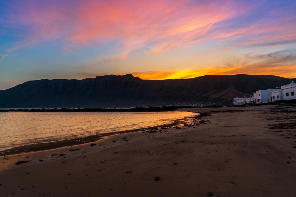 a sunset on a beach with a mountain in the background at VolcanoKite Apartments in Famara