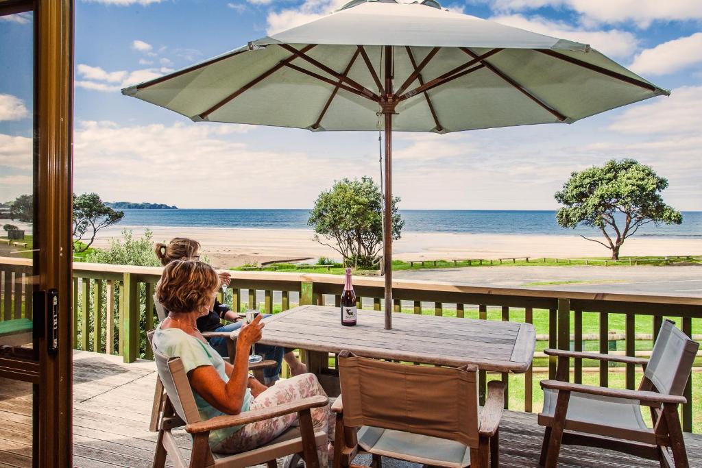 a woman sitting at a table with an umbrella at Sandy Bay Beachfront in Matapouri