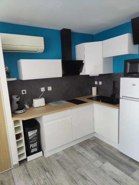 - une cuisine avec des placards blancs et des murs bleus dans l'établissement Studio climatisé 50 m.du port, à Saint-Cyprien