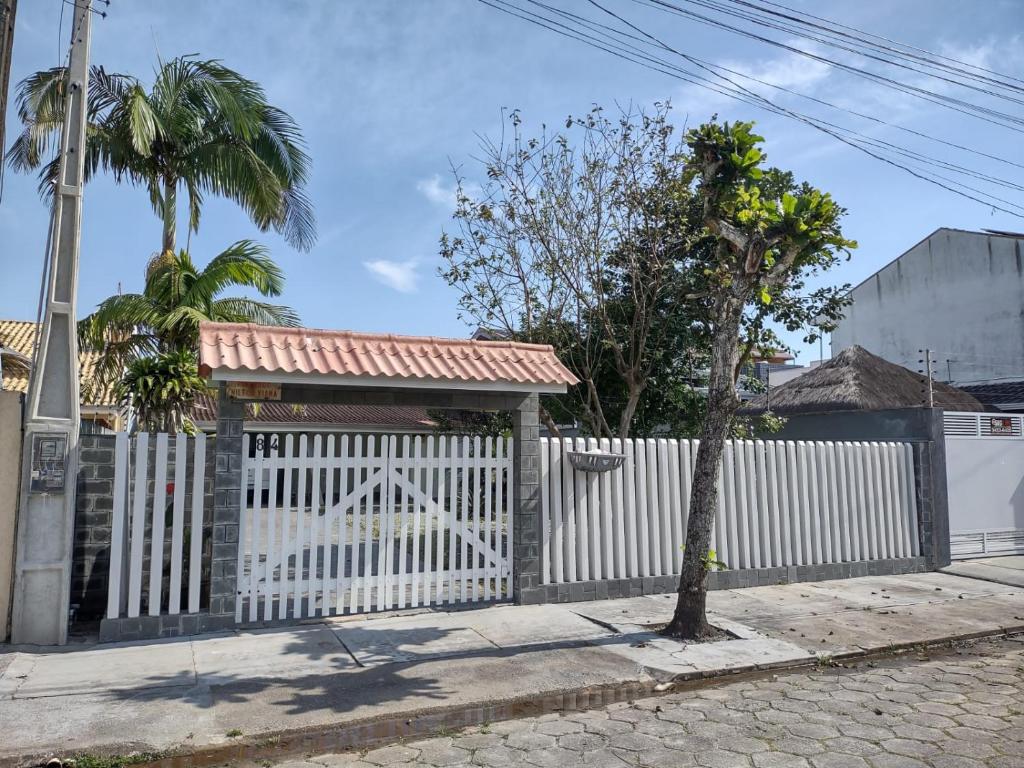 una cerca blanca con una puerta y una palmera en Casa 50m do mar, en Matinhos