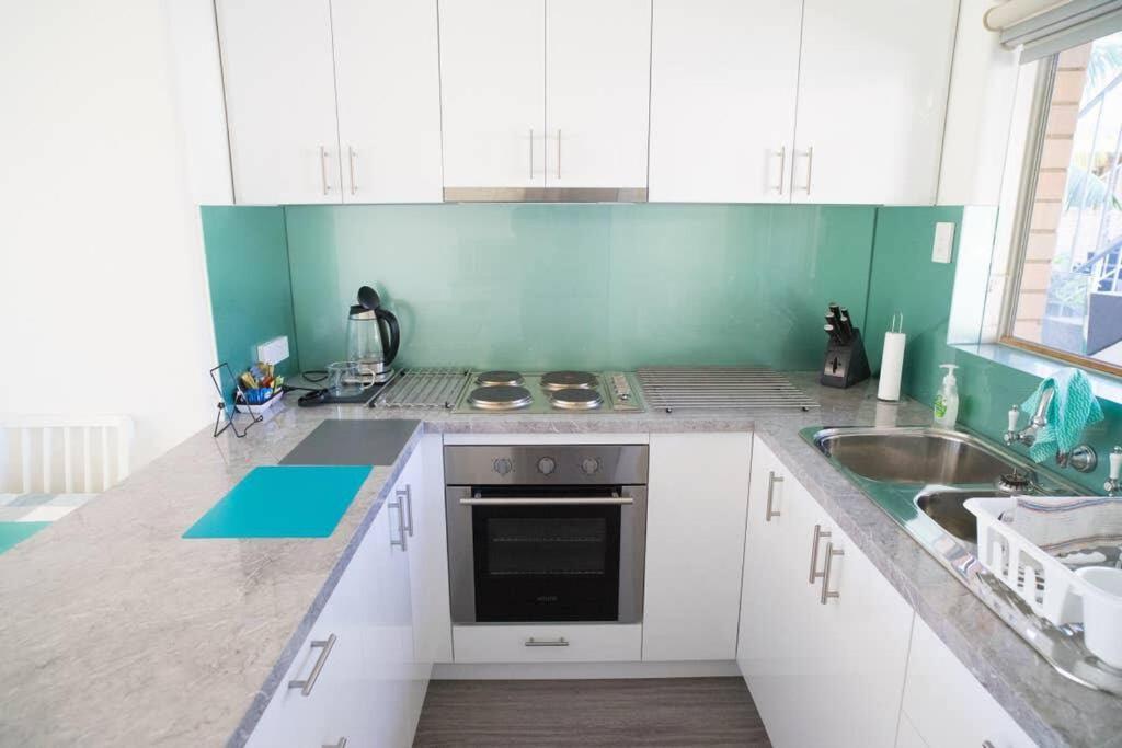 uma cozinha com armários brancos, um fogão e um lavatório em 6 Sand Sun & Surf 1br 1 Bth em Perth