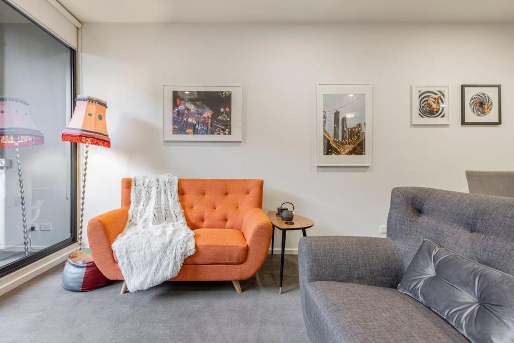 sala de estar con silla naranja y sofá en City-edge Living in Trendy North Melbourne en Melbourne