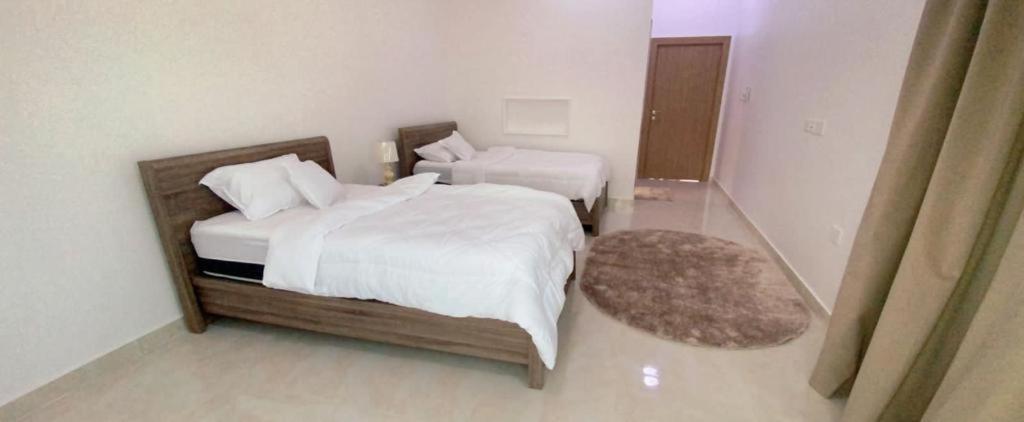 1 dormitorio con 2 camas con sábanas blancas y alfombra en دار الضباب dar al dhabab 