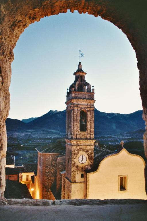 a church with a clock tower in front of a building at Casa Rosa in Alcalalí