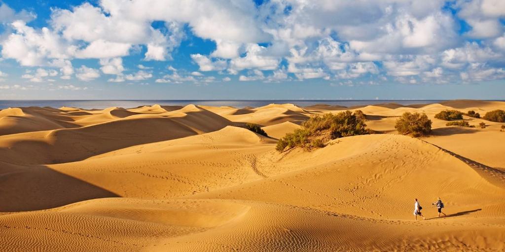 dos personas caminando por las dunas de arena en el desierto en FABULOUS BUNGALOW , WIFI, SWIMMING POOL AND BEACH en Pasito Blanco