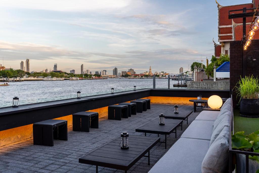 A rooftop riverside dining terrace with low tables and a wide Bangkok skyline view.