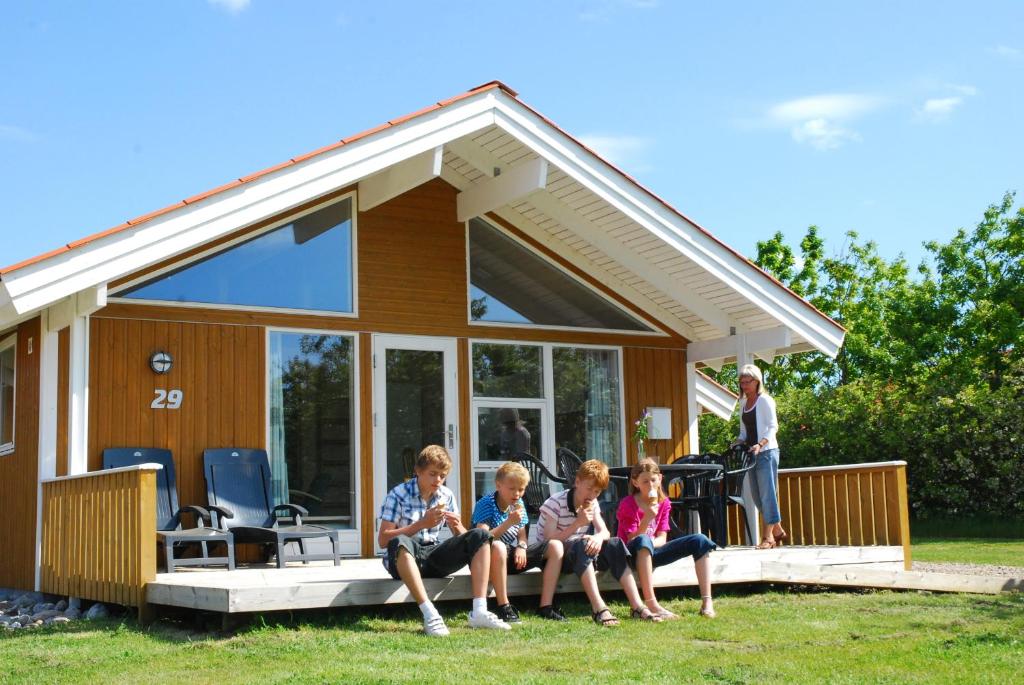 drei Kinder sitzen auf der Veranda eines winzigen Hauses in der Unterkunft Skærbæk Holiday Center in Skærbæk