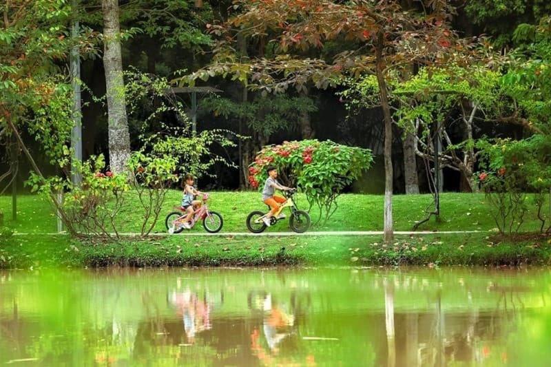 dwoje ludzi jeżdżących rowerami w parku obok stawu w obiekcie Ecopark Happy Haven w mieście HÆ°ng YÃªn