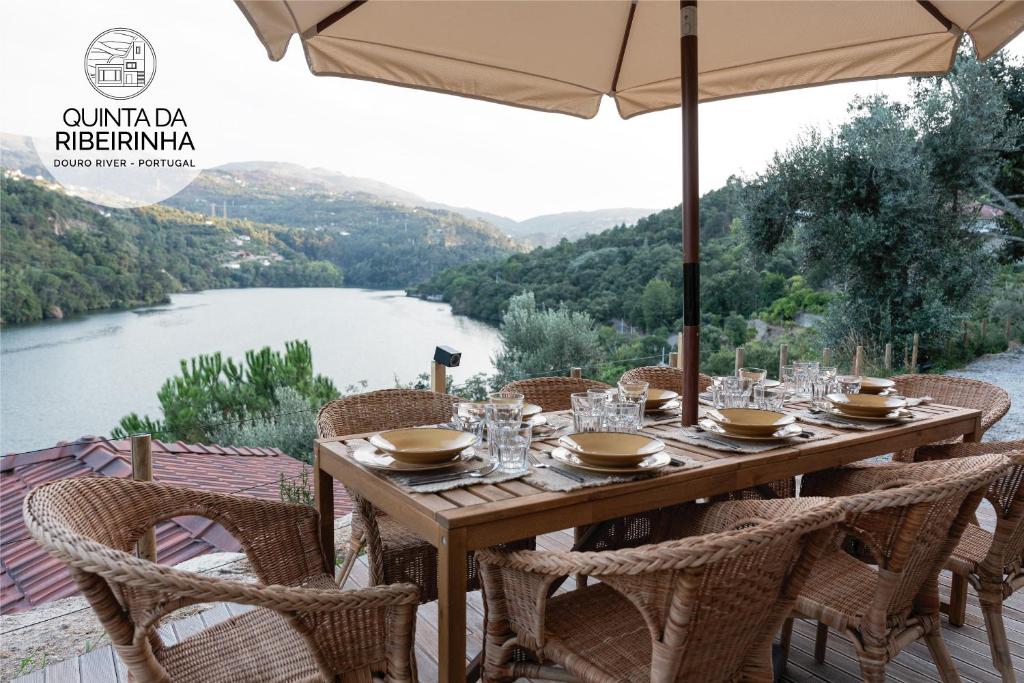 uma mesa de madeira com cadeiras e um guarda-sol com vista para um rio em Quinta da Ribeirinha - Douro River em Paços de Gaiolo