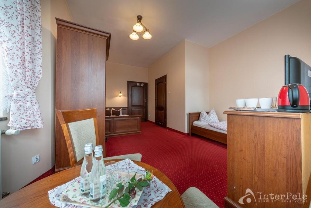 Spacious guest room with table, bottled water, red carpet, kettle on wooden cabinet.