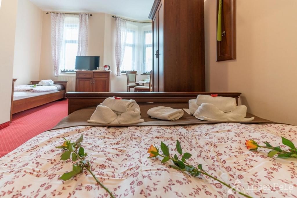 Flower-adorned bed in hotel room with folded towels on footboard, wardrobe and windows in background.