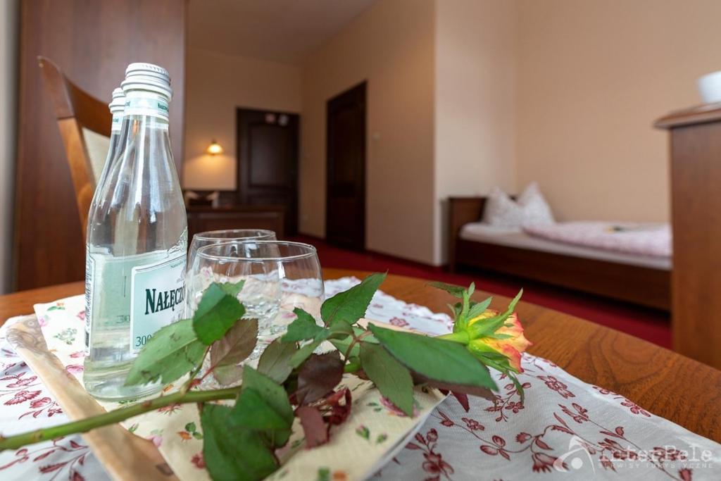 Table with bottled water, two glasses and rose, blurred bed in background suggesting welcome.
