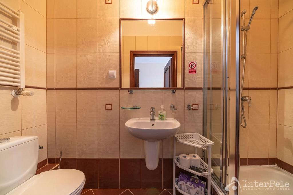 Compact bathroom with sink, mirror, shower cubicle and toilet against beige tiled walls.