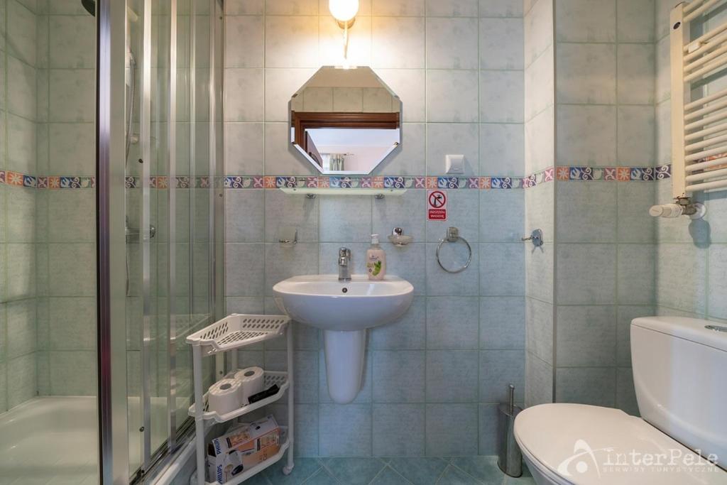 Small tiled bathroom with glass shower, pedestal sink, mirror and white toilet.