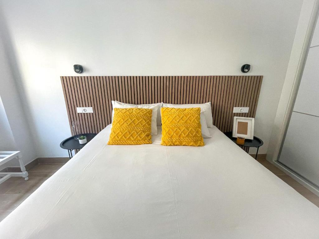 uma grande cama branca com almofadas amarelas num quarto em H&H Suite El Mirlo em Granada