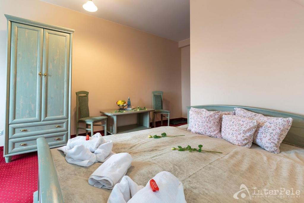 Light bedroom with green-painted bed, floral pillows, towels arranged and roses on beige cover.