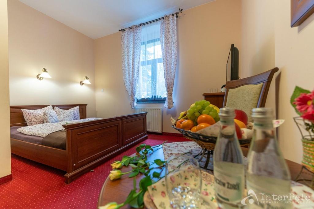Cozy bedroom view showing wooden bed, bedside table with fruit basket and bottled water.