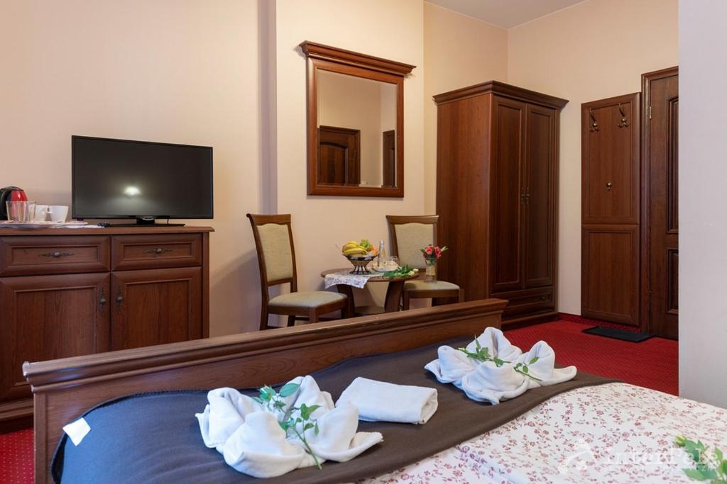 Guest room seating area with table, chairs, TV, wardrobe and folded towels on bed.