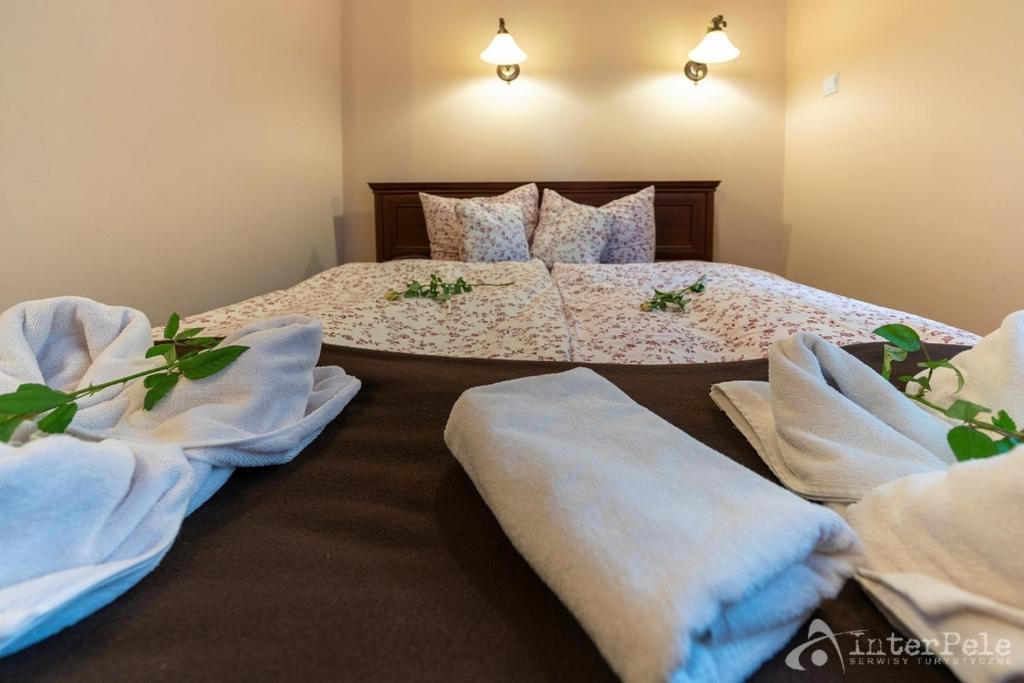 Bed foreground with folded towels, floral duvet, decorative green sprigs and warm wall lighting.
