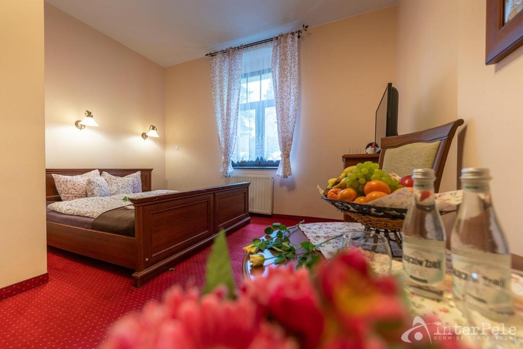 Cozy hotel bedroom with wooden double bed, red carpet, fruit basket and bottled water on table.