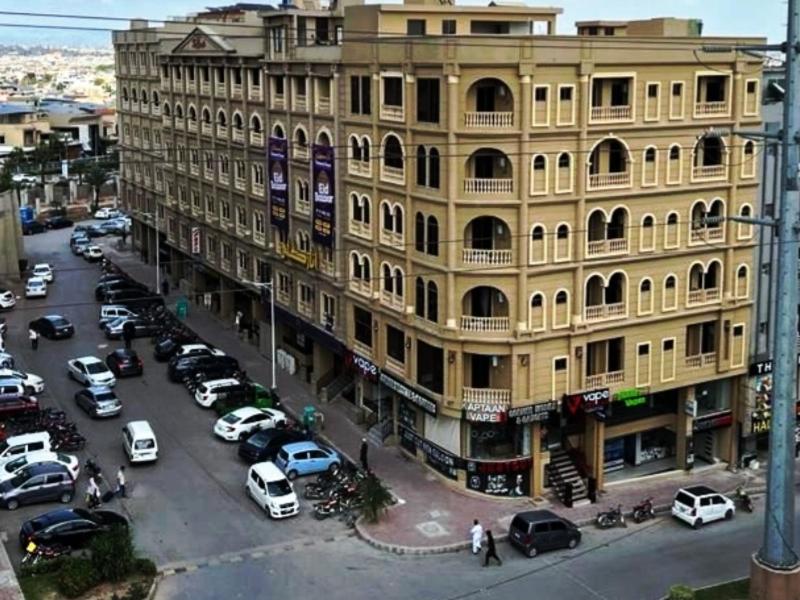 un grand bâtiment jaune avec des voitures garées dans un parking dans l'établissement Northern Suites Bahria town, à Rawalpindi