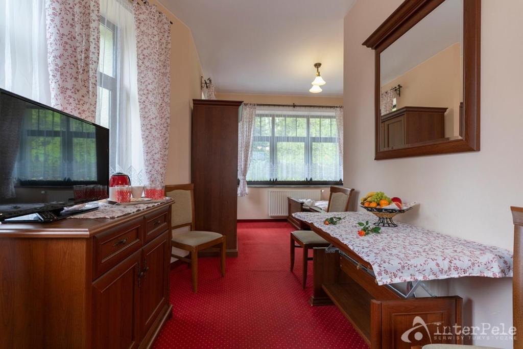 Cozy hotel sitting area with wooden furniture, TV, floral curtains, table with fruit and bench.