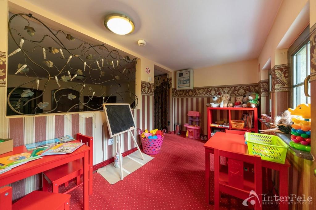 Children's playroom with red tables, toys, bookshelves, chalkboard easel, and stuffed animals.
